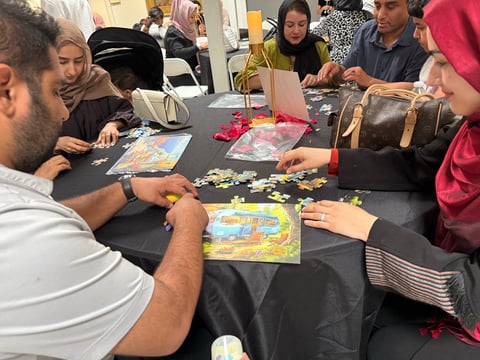 Group of people assembling jigsaw puzzles together around a black table at an indoor gathering