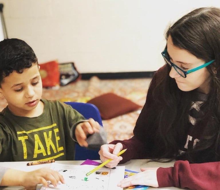 Woman wearing glasses helps young boy with art project on table indoors