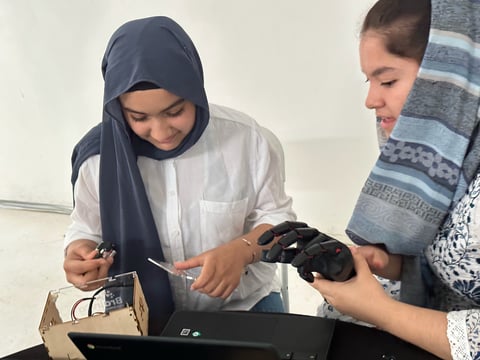 Two women examining a black VR headset together, with one wearing a hijab and white shirt