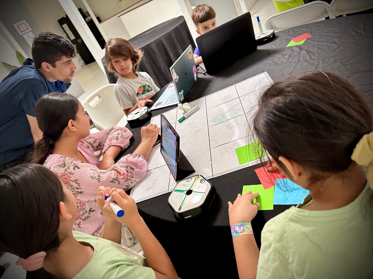 Group of students gathered around a table working on a project with laptops and colorful sticky notes
